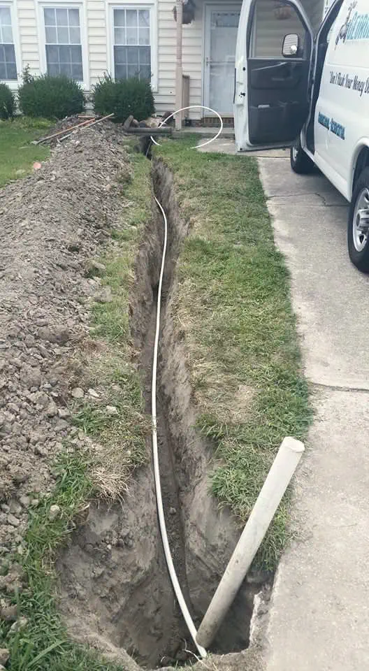 A new white water line laid in an open trench along a front walk, with the George's Plumbing van behind